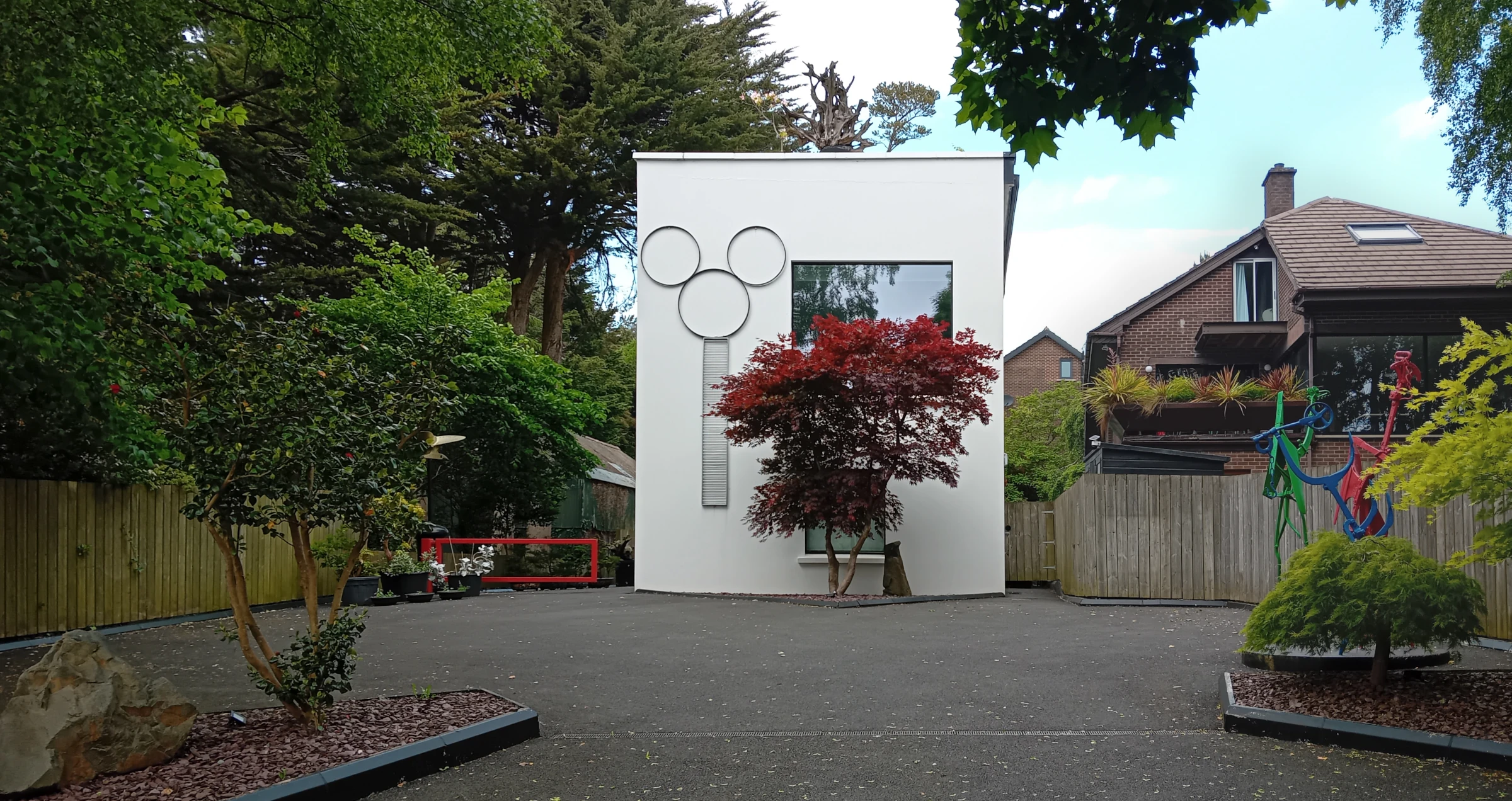Front garden view of Long House / The Gallery, a contemporary white house in Belfast with circular façade details and a red maple tree.