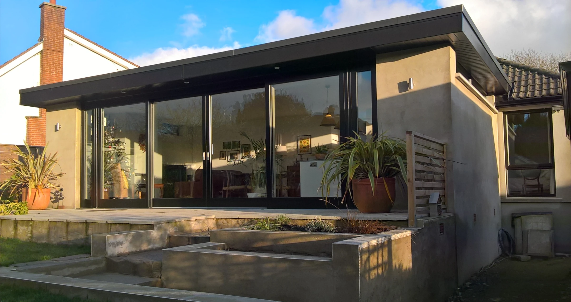 Modern rear extension to a bungalow with raised patio and large sliding glazed doors, viewed from the garden.