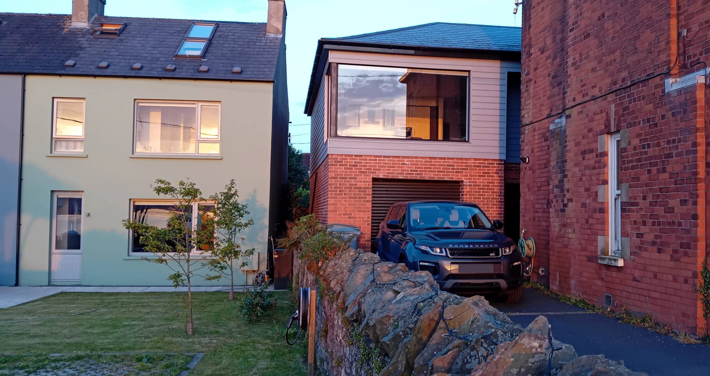Substantial extension to an existing red-brick house, with upper-floor living space, large picture window and garden boundary wall.